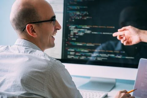 Programmer, working behind the desk, analysing code while chatting with cowor Stock Photos