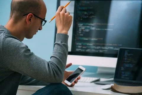 Programmer, working behind the desk, analysing code on the black screen. Stock Photos