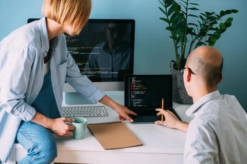 Programmer, working behind the desk, analysing code while chatting with cowor 库存照片