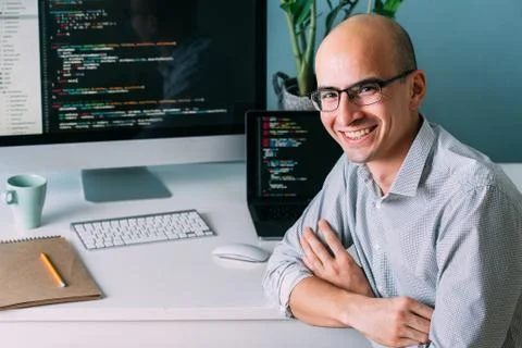 Programmer, working behind the desk, with two screens filled with code lines Stock Photos