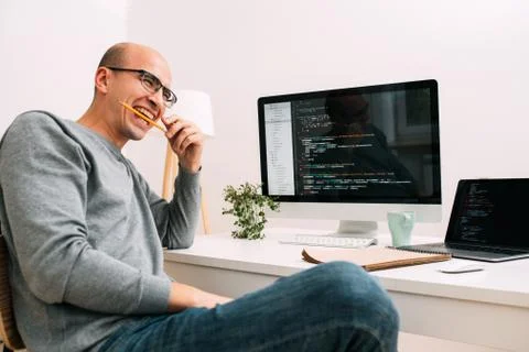 Programmer, working behind the desk, with two screens filled with code lines 스톡 사진