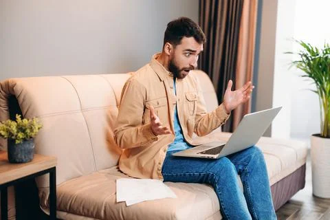 Programmer working from home is shocked reading work chat. Young bearded man in Stock-Fotos