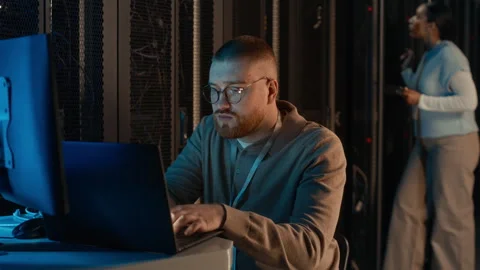 Programmer Working on Laptop in Server Room with Female Colleague Stock Footage 311309280