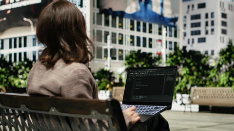 Programmer writing code on laptop while sitting on park bench outdoors Video stock 343557193