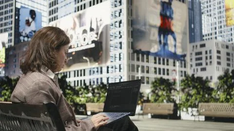 Programmer writing code on laptop while sitting on park bench outdoors Stockfoto's