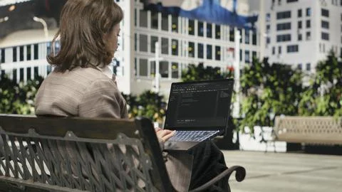 Programmer writing code on laptop while sitting on park bench outdoors Stockfoto's