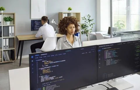 Programmers and developers coding software on multiple monitors in bright office Stock Photos