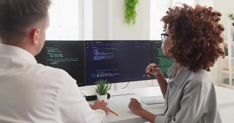 Programmers collaborating at dual monitors reviewing code in modern bright Stock Footage 337928721