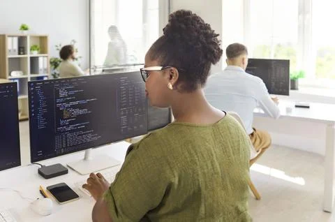 Programmers collaborating at modern office desks with code on dual monitors 库存照片