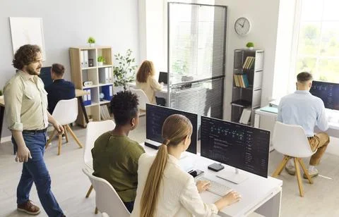 Programmers collaborating in open office workspace, coding software on computers 스톡 사진