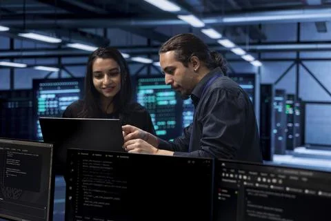 Programmers in data center using laptop to check for server performance issues Foto stock