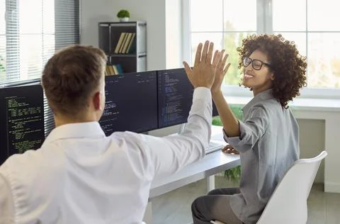 Programmers give high five after fixing code in bright tech office modern Foto stock