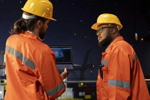 Programmers on offshore oil platform deck using AI on laptop Stock-Fotos