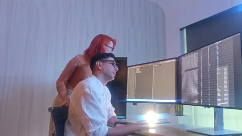 Programmers working at night analyzing code on monitors in a modern office. Stock Footage 333998979