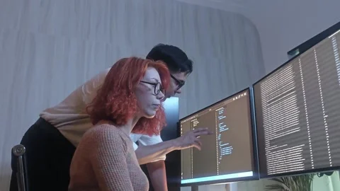 Programmers working at night analyzing code on monitors in a modern office. Stock Footage 333999017