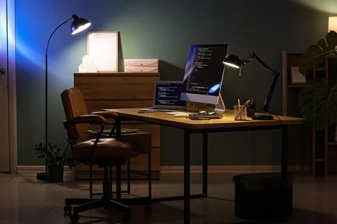 Programmer's workplace with computer and glowing lamps in dark office interio Stock Photos