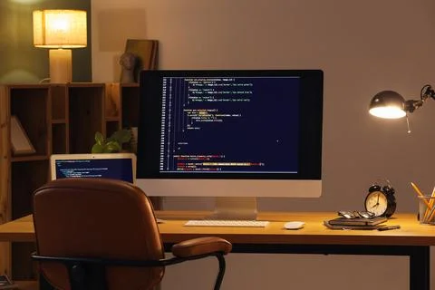 Programmer's workplace with computer and glowing lamp in dark office Stock-Fotos