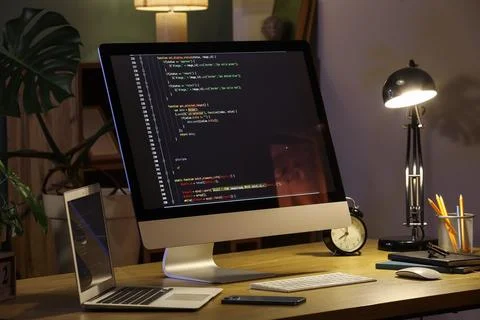 Programmers workplace with computer, laptop and glowing lamp in dark office 스톡 사진