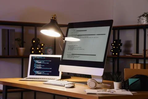 Programmer's workplace with computer, laptop and glowing lamp in office Stock Photos