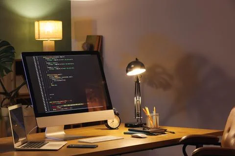 Programmer's workplace with computer, laptop and glowing lamp in dark office Stock-Fotos