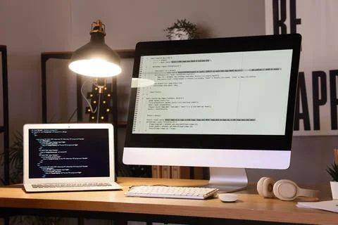 Programmers workplace with computer, laptop and glowing lamp in office 스톡 사진