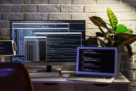 Programmer's workplace with gadgets and plant near grey brick wall in dark of Stock-Fotos