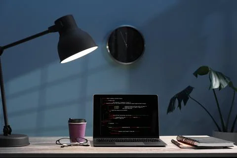 Programmer's workplace. Modern laptop with unfinished code, lamp and other .. Stock Photos