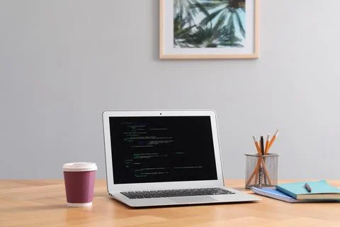 Programmer's workplace. Modern laptop with unfinished code, paper cup of dr.. Stock Photos