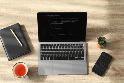 Programmer's workplace. Modern laptop with unfinished code, smartphone and .. Stock Photos