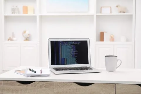 Programmer's workplace. Modern laptop with unfinished code, cup and station.. 库存照片