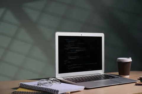 Programmer's workplace. Modern laptop with unfinished code, notebooks, glas.. 库存照片