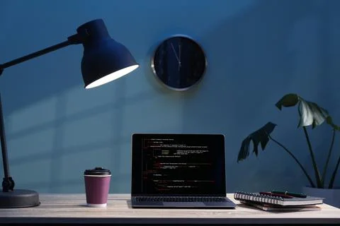 Programmer's workplace. Modern laptop with unfinished code, lamp and other .. Stock Photos
