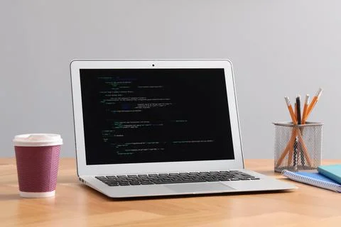 Programmer's workplace. Modern laptop with unfinished code, paper cup of dr.. Stock Photos
