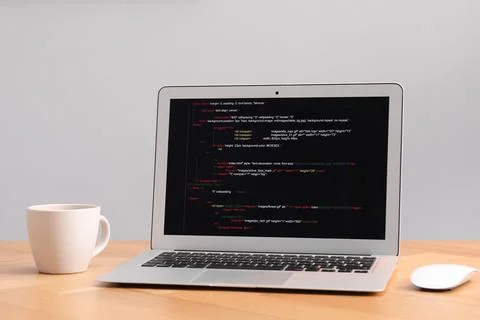 Programmer's workplace. Modern laptop with unfinished code and cup on desk .. Stock Photos