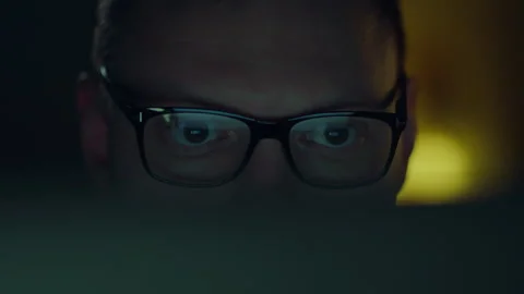 A programming specialist is deep in work at night, the reflection of a flick Vidéo 259706683