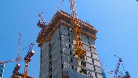 An in-progress high-rise, ringed by yellow cranes, shows exposed floors. Stock Photos
