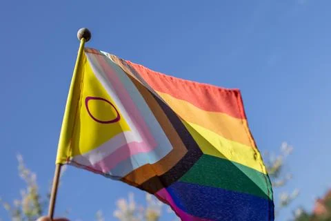 Progress Pride Flag featuring intersex symbol flying outdoors in sunlight a.. Stock Photos
