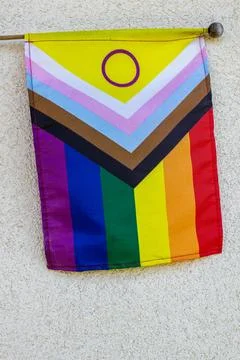 Progress Pride Flag with intersex circle hanging on a white wall. Stock Photos