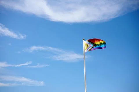 Progress pride flag waving on a flagpole against blue sky with clouds Stock Photos