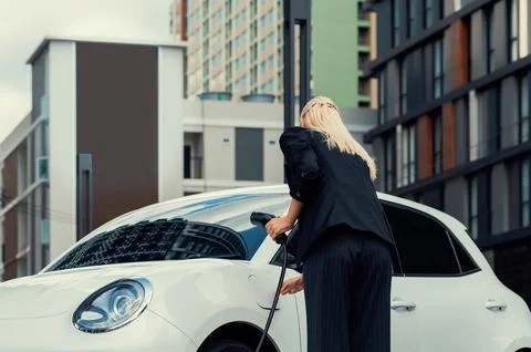 Progressive businesswoman plugs charger plug from charging station to EV. Stock Photos