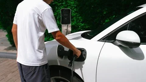 Progressive man install cable plug to his EV car from home charging station. Stock Photos