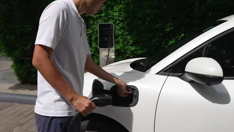 Progressive man install cable plug to his EV car from home charging station. Stock Photos