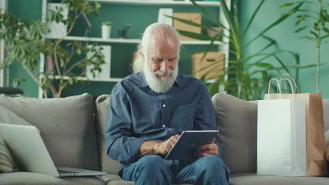 Progressive Senior Man is Sitting on the Sofa with Paper Box at Home Stock Footage 196250908