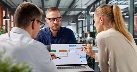 Project Manager Guides Diverse Team Using AI Tools On Laptop Daily. Stock Photos