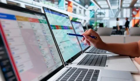 Project Manager Updates Agile Task List On Laptop During Busy Office Meeting. Stock Photos