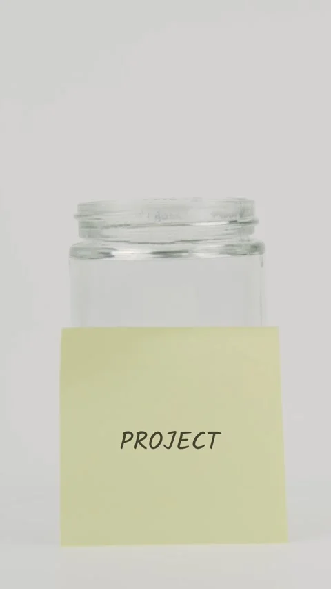 Project text or word on yellow sticky note attached to glass jar with hand Stock Footage 311771663