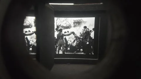 A projector displays black-and-white wartime photos in a dark museum room. Stock Footage 337116749