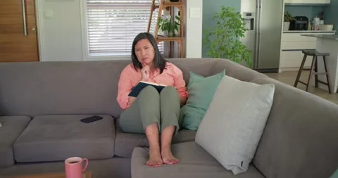 Prompted by open blue notebook, mature female writing in living room, pausing Stock Footage 337933049