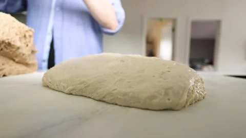 Proofed bread dough on floured kitchen counter while blurred baker shapes dough Stock Footage 339306708