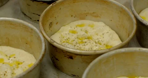 Proofed dough in round metal pans with oil pools and herb flecks in bakery Stock Footage 344583383